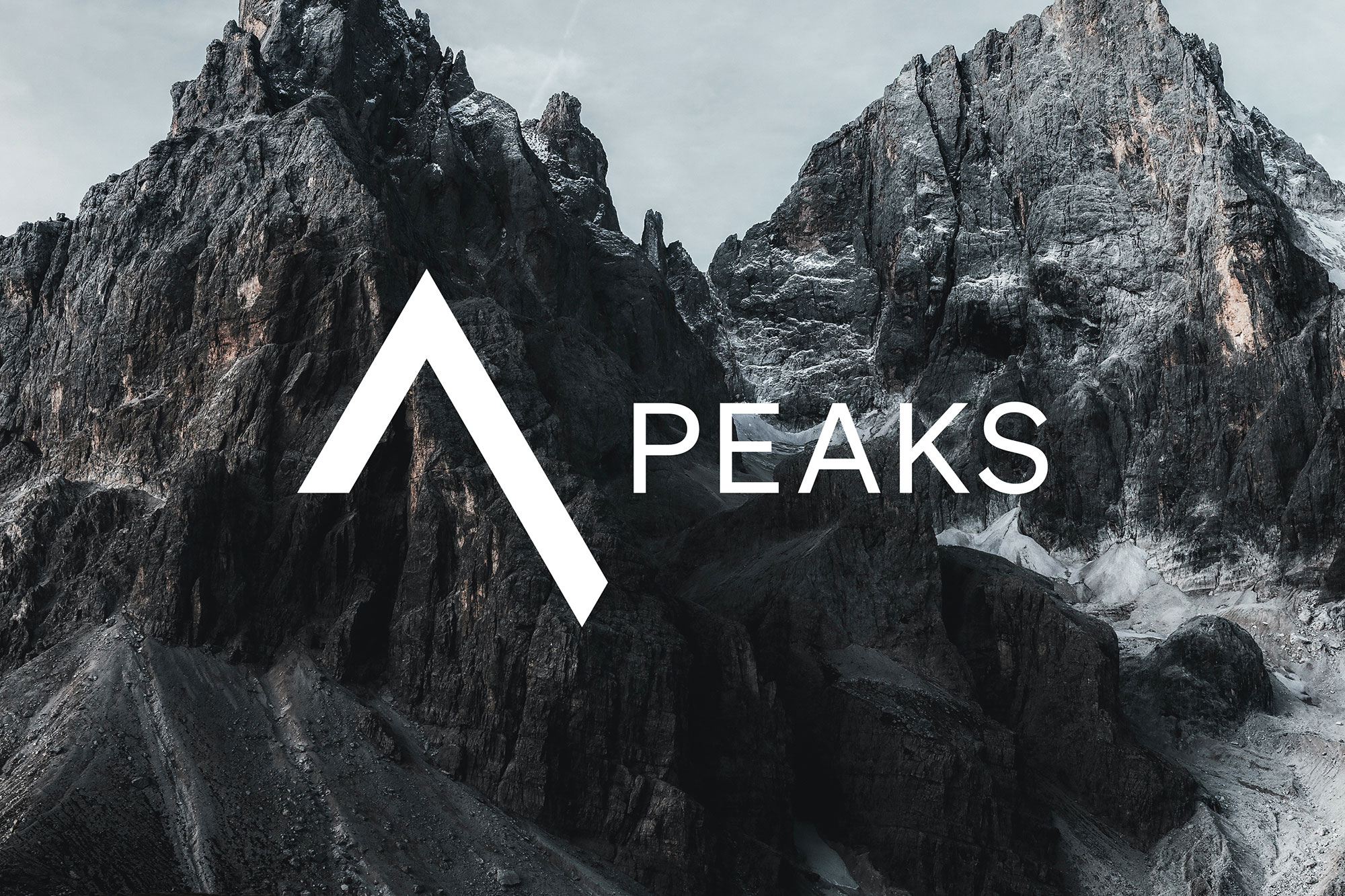 weißes Seven Peaks Logo auf einem Foto, das die dunkelgraue bis schwarze Gesteinslandschaft von Berggipfeln zeigt