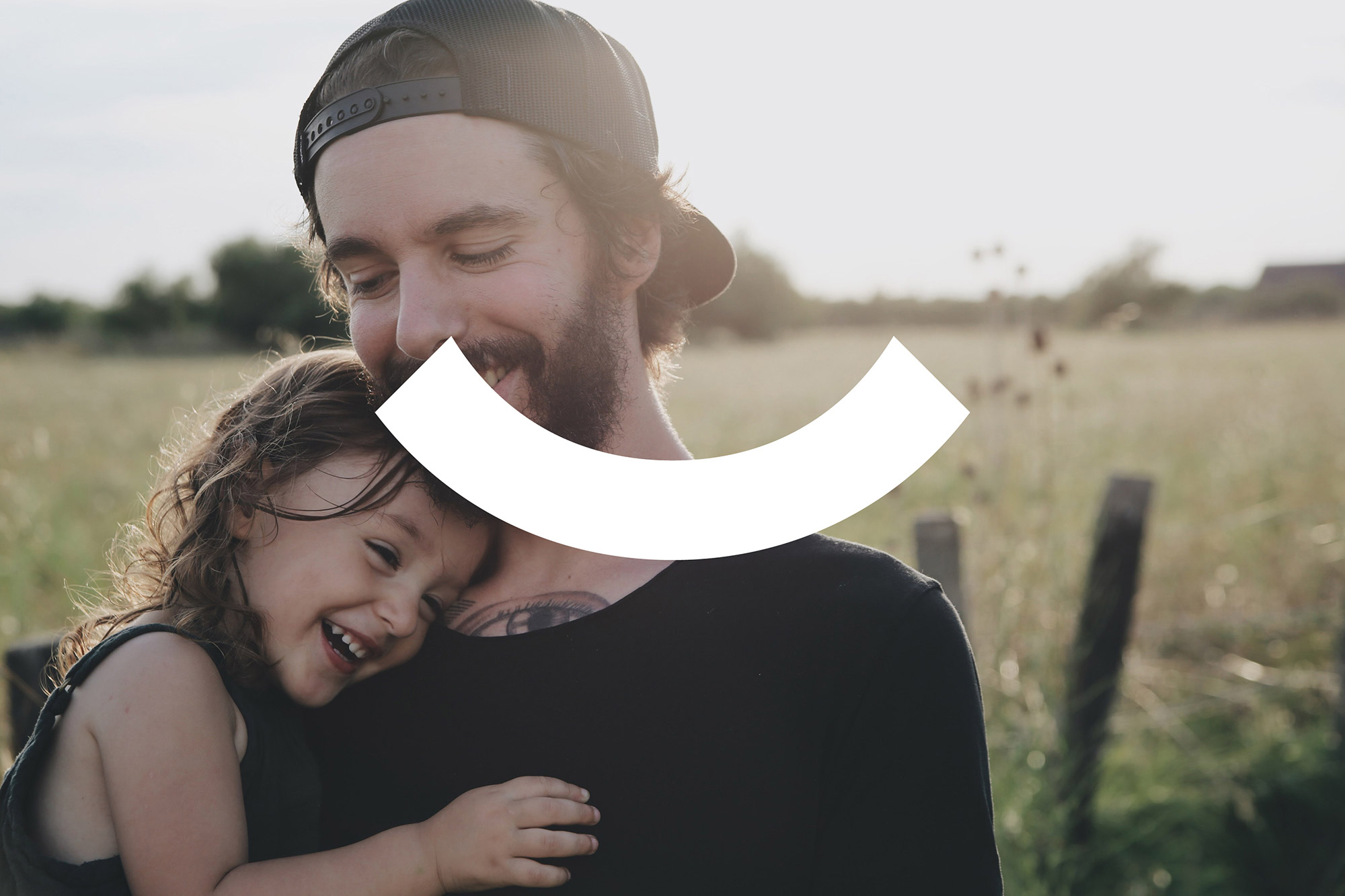 weißes Oberbillwerder Logo auf Fotografie von einem Vater der seine kleine Tochter auf dem Arm hält. Beide lächeln und stehen in einer grünen Wiesenlandschaft an einem warmen Sommertag.