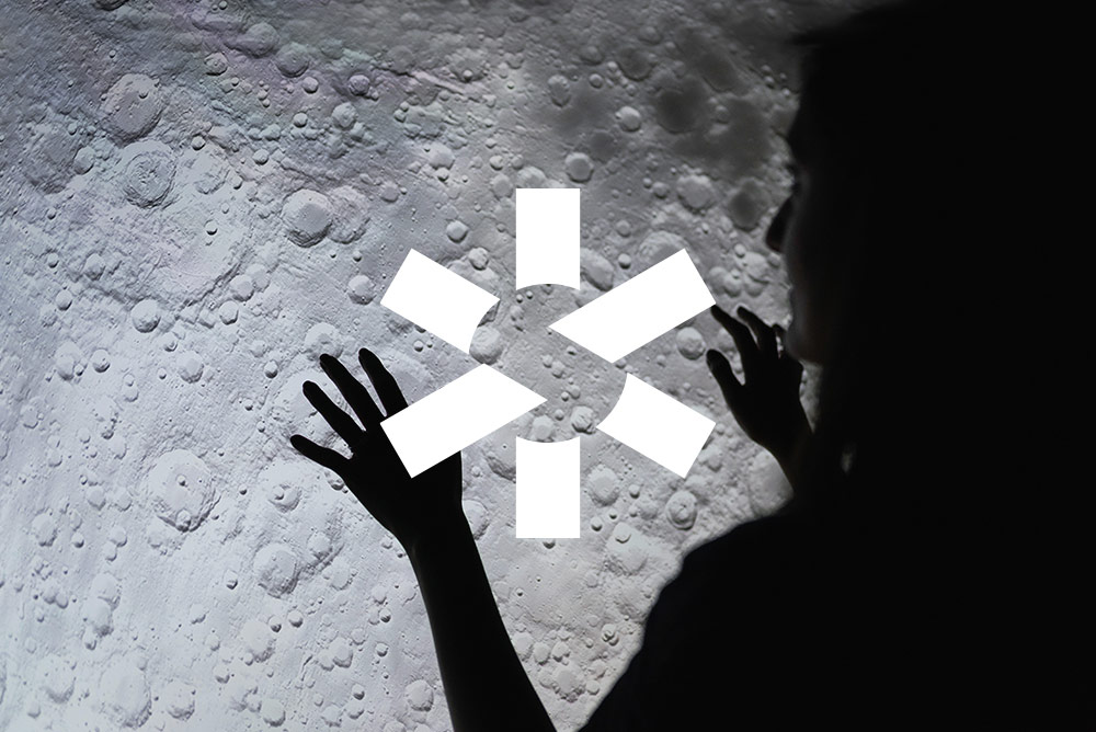weißes Science City Logo auf schwarz-weiß Foto, dass im Gegenlicht eine Person zeigt, die ihre Hände auf das erleuchtete Bild einer Mondlandschaft legt