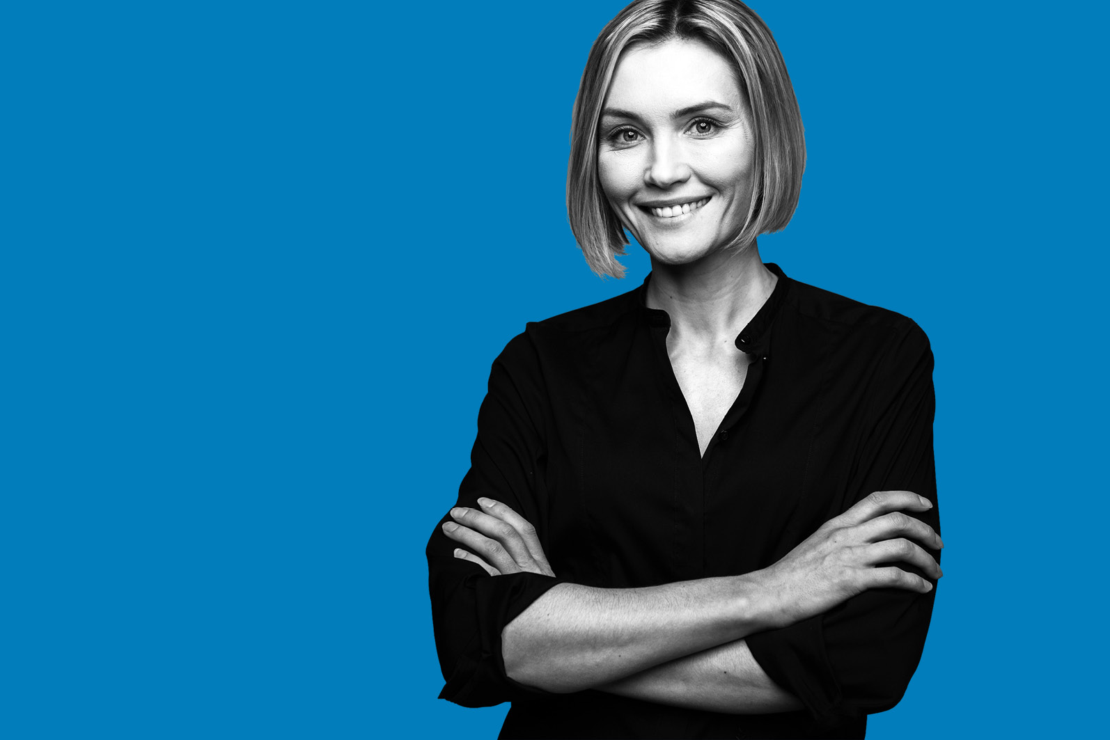 black and white image of smiling woman with crossed arms against blue background.